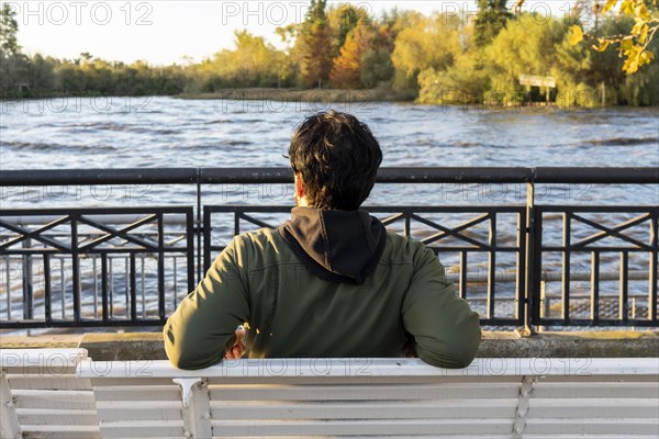 Back view of a man sitting on a bench at sunset contemplating the river