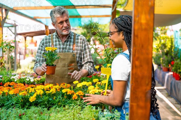 Happy black ethnicity female customer buying flowers from gardener in nursery inside greenhouse