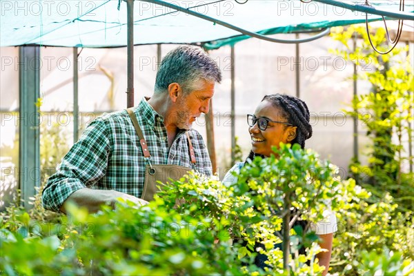 Master gardener teaching flower nursery student girl checking plants in greenhouse