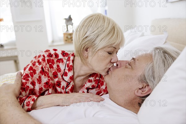 Older couple lying together in bed in bedroom and kissing