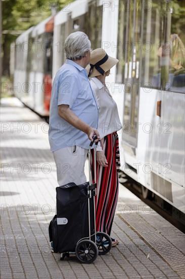 Elderly couple waiting with a trolley at a stop for the tram