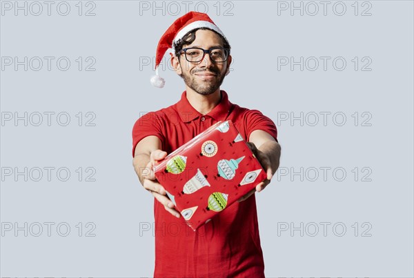 Smiling guy in christmas hat offering you a christmas gift box. Christmas man offering a gift boxes isolated. Handsome man in christmas clothes showing a gift box