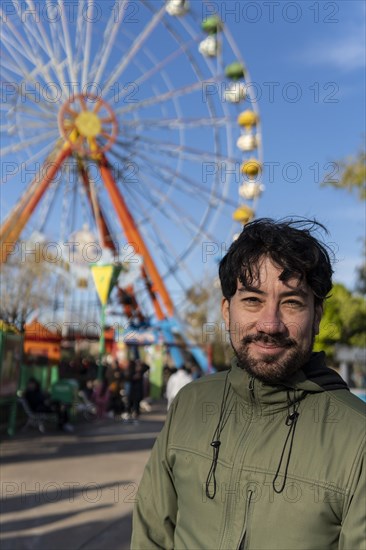 Portrait of latino man in an amusement park posing happy with the ferris wheel in the background