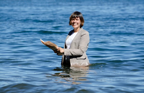 Elegant Business Woman with Suit Standing in the Water and Reading a Newspaper