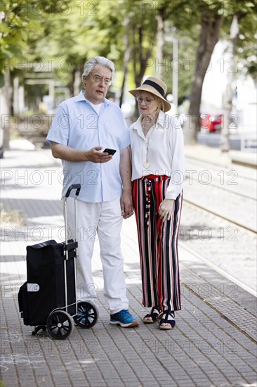 Elderly couple waiting for the tram at a stop with a smartphone in hand