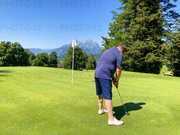 Golfer on Putting Green with Mountain and the Moon View in a Sunny Summer Day in Burgenstock
