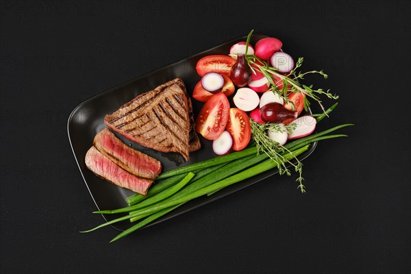 Top view of grilled tri-tip loin beef steaks medium rare with fresh vegetables on black background