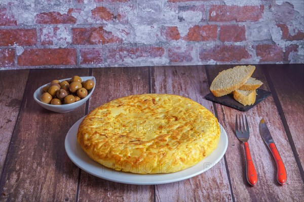 Typical spanish potato omelette freshly made on a wooden table with cutlery