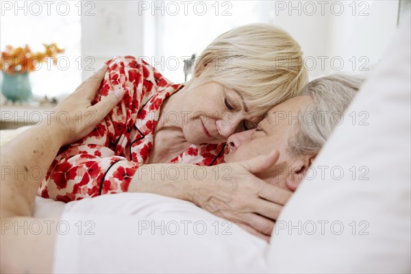Elderly couple lying together in bed in bedroom embracing tenderly