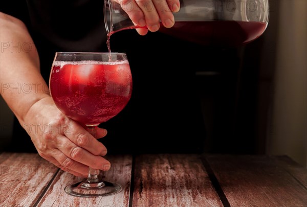 Waitress dressed in black serving a glass of sparkling red summer wine on the rocks from a glass decanter