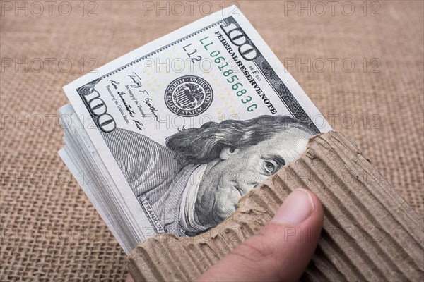 Hand holding banknote bundle of US dollar on a linen canvas background