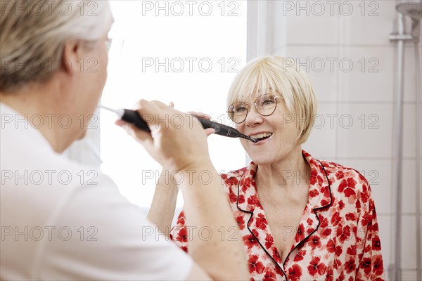 Elderly couple brush their teeth together in the bathroom