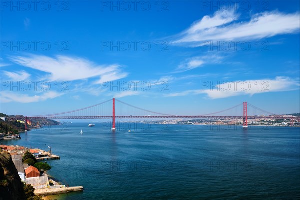 View of 25 de Abril Bridge famous tourist landmark of Lisbon connecting Lisboa to Almada on Setubal Peninsula over Tagus river with boats yachts and vessels. Lisbon