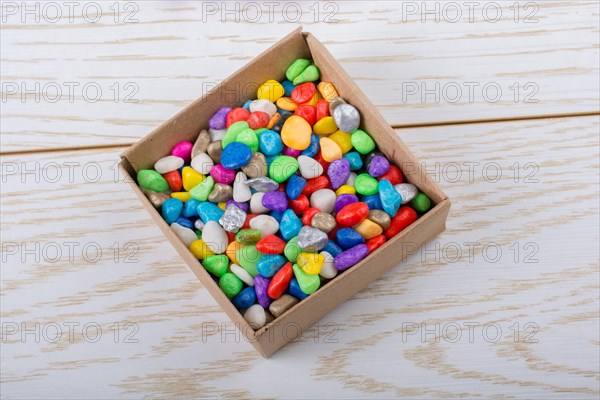 Little colorful pebbles in a box on wooden texture