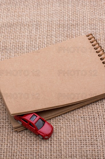 Red toy car coming out of a notebook on a linen canvas