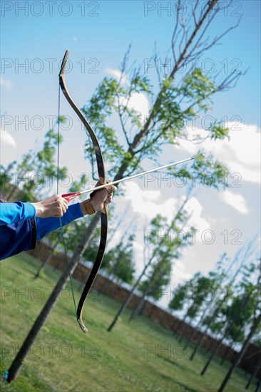 Archer with bow in traditional clothes shooting an arrow