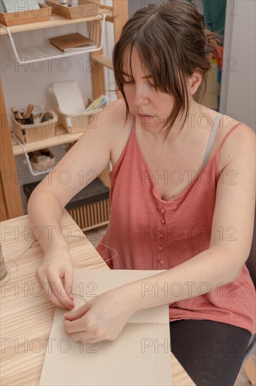 Young brunette girl with long hair craftswoman working on her products in her home workshop sewing notebooks