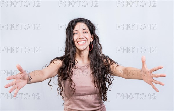 Happy young latin woman welcoming with open arms isolated. Hospitable girl opening arms to the camera. Smiling girl asking for a hug