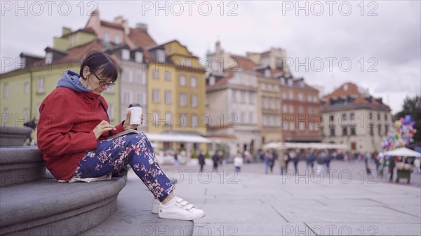 Elderly lady sits on the steps drinking coffee and using a smartphone in the historic center of an old European city. Palace Square