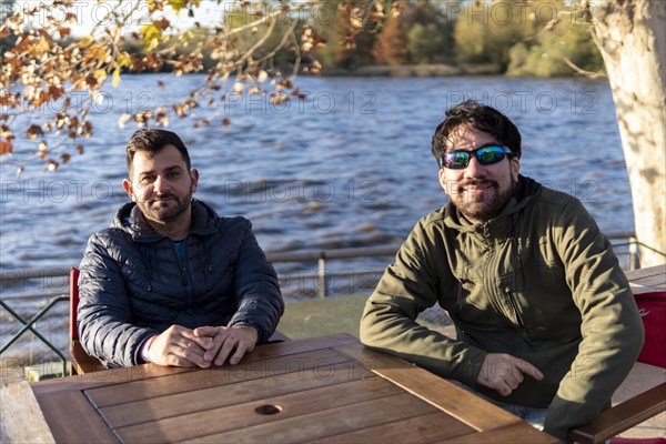 Two friends sitting at an outdoor bar on a river at sunset