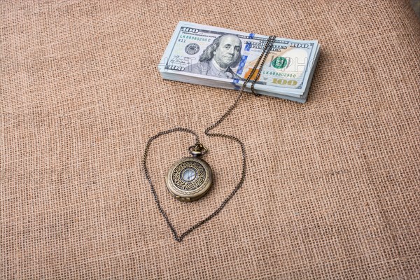 Pocket watch wrapped around bundle of US dollar forms a heart