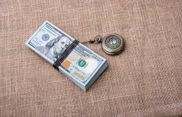 Pocket watch wrapped around banknote bundle of US dollar