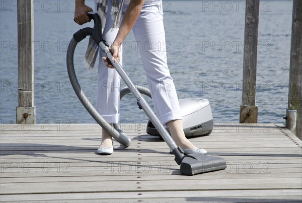 Woman Using Vacuum Cleaner the Pier over the Alpine Lake with Cleaning Equipment in Switzerland