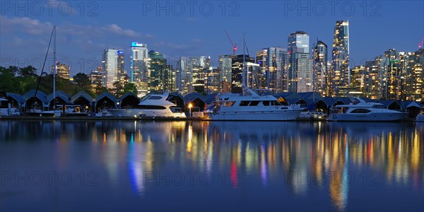 Illuminated skyscrapers and pleasure boats reflected in the calm water