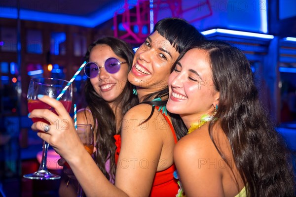 Portrait female friends in a nightclub dancing with the glasses at a summer night party in a pub