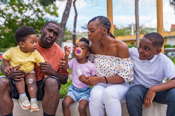 African black ethnic family with children in playground blowing soap bubbles