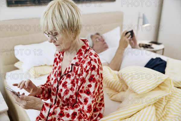 Elderly couple together in the bedroom and each looking at their own smartphone