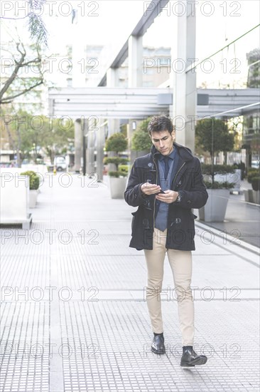 Portrait of businessman walking in the street texting with his phone