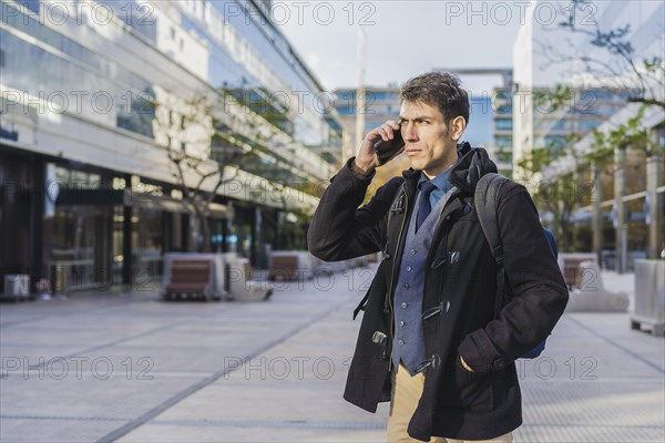 A handsome businessman is talking on the cell phone near his office. Copy space