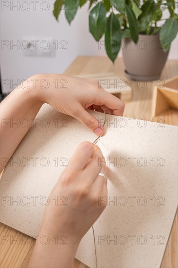 Close-up detail of woman's hands sewing a handmade notebook made in her workshop