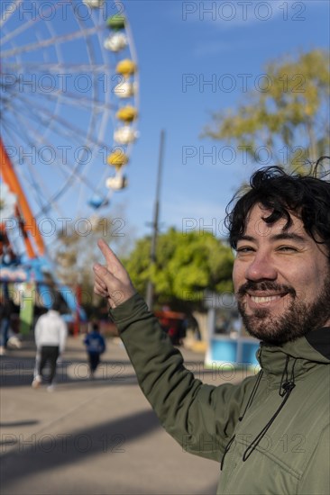 Portrait of latino man in an amusement park posing happy with the ferris wheel in the background