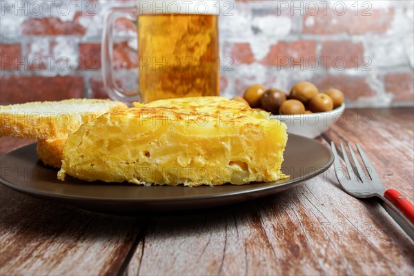 Typical spanish potato omelette freshly made on a wooden table with a fresh pitcher of beer