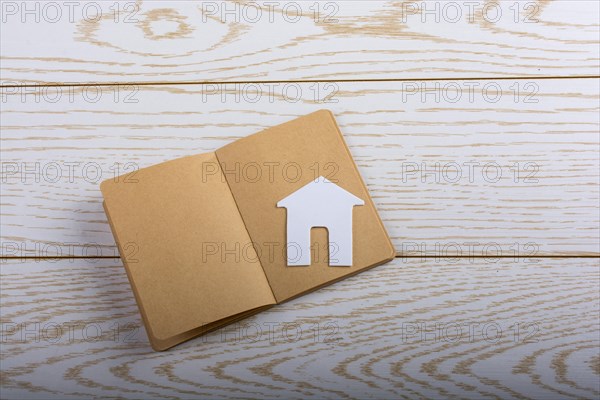 Little paper house on a notebook on parquet