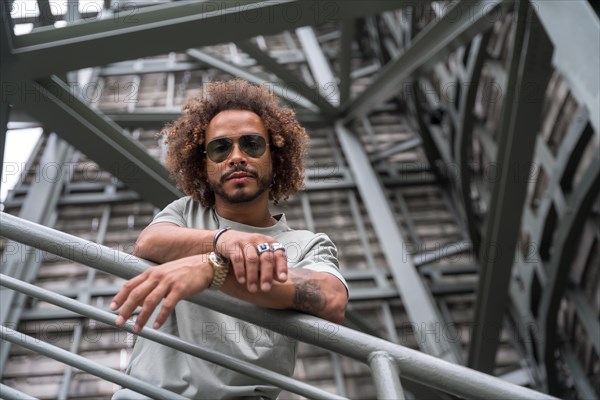 Portrait of a young man with afro hair wearing sunglasses on the stairs in the city