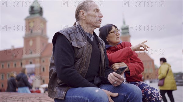 Elderly couple of tourists are sitting and talking in the historic center of an old European city