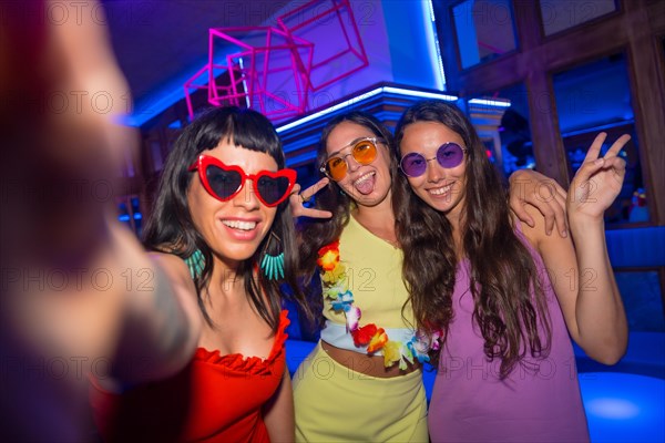 Friends in a nightclub taking a selfie with the phone at a night party on summer vacation in a pub