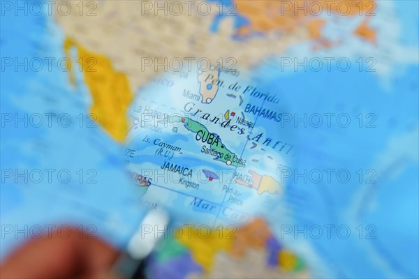 Hand of a man with a magnifying glass looking at cuba on a map of the world