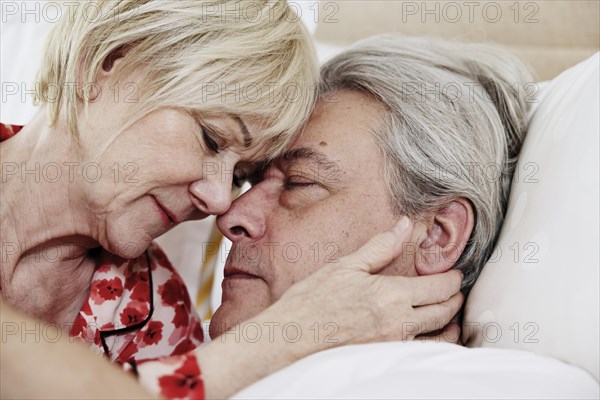 Elderly couple lying together in bed in bedroom embracing tenderly