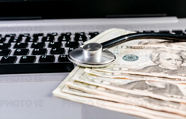 Stethoscope on top of money on laptop keyboard. Stethoscope on dollar bills on top of laptop keyboard