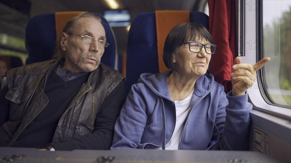 Elderly couple is riding in a train carriage and looking out the window and talking with each other