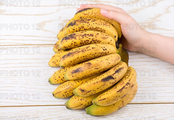 Hand holding bunch of freckled bananas on a wooden texture