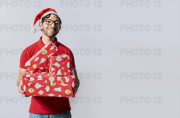 Christmas man portrait holding gift boxes and smiling isolated. Smiling guy in santa hat holding christmas gift boxes. Friendly man in christmas clothes holding gift boxes isolated