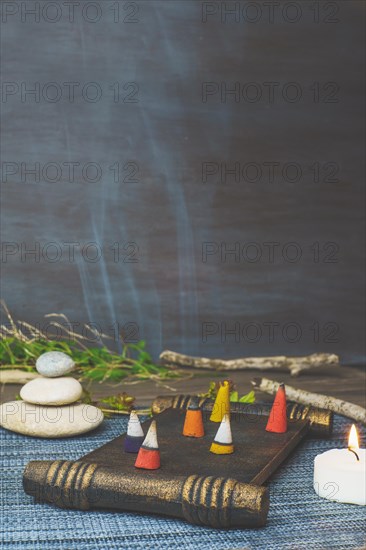 Colorful incense cones burning and smoking on a wooden tray with stacked zen stones