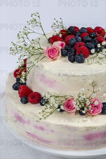 Summery fresh two tier wedding cake decorated with berries and flowers festive cream cake on light background