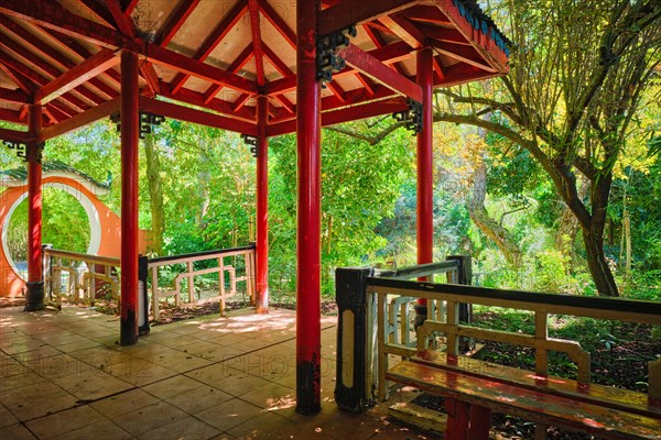 Red Chinese style pavilion in lush greenery of asian part of tropical botanical garden in Lisbon