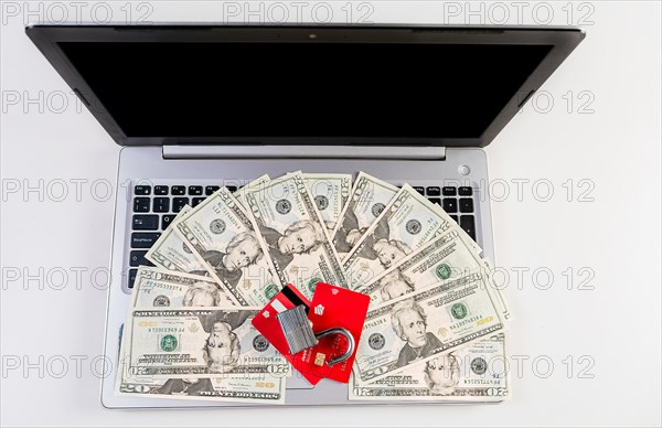 Top view of padlock with credit card on top of dollars on laptop keyboard. Padlock on top of credit card over dollar bills on computer keyboard